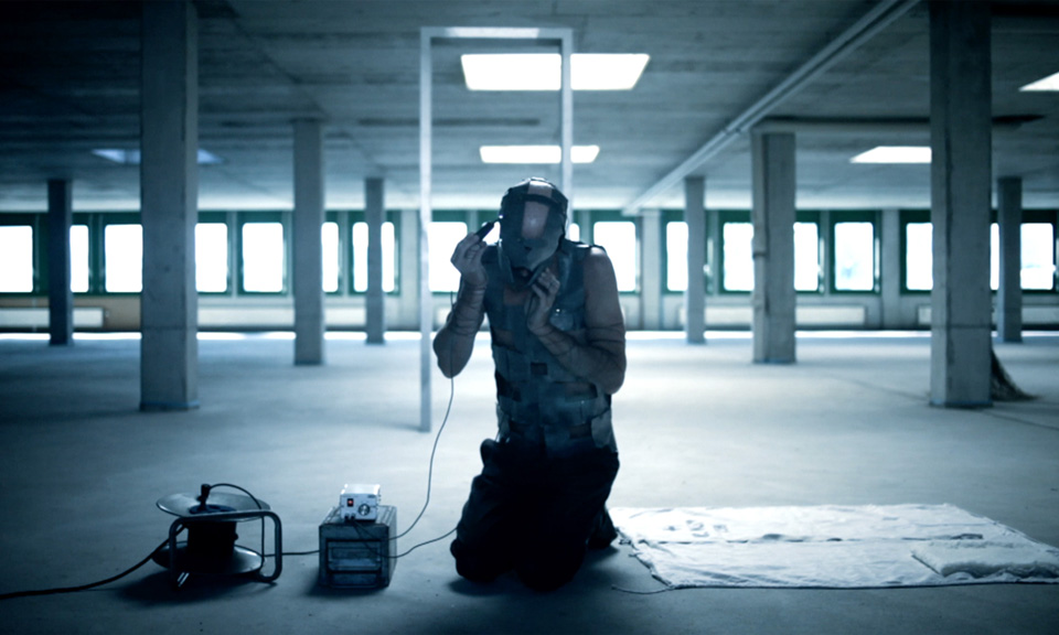 Blue-tinted interior photo with a seated figure and luggage in an empty parking structure.